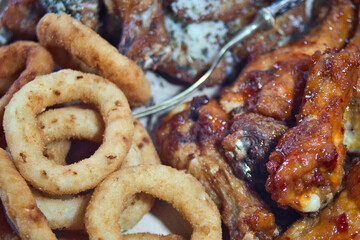 Delicious and unhealthy fast food - deep fried chicken wings with sweet chili sauce and parmesan with basil served with onion rings