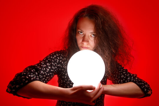 Fortuneteller Holding A Glowing Ball In Her Hands. Red Background.