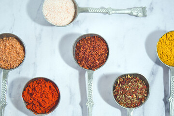 Assortment of kitchen herbs and spices on the marble table - saffron, chili pepper, paprika, pink Himalayan salt, tomato salt and mixed Indian herbs