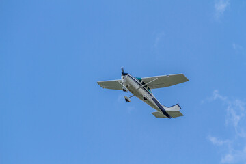 A small light light plane aircraft flies in a clear blue sky. Horizontal orientation. 