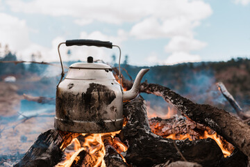 Boiling water on a camping trip with fire in the mountains, cooking on a fire with firewood. Kettle...