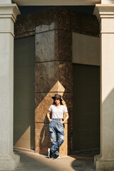 Obraz na płótnie Canvas Attractive young Vietnamese woman in jeans and white t-shirt standing in sunlight at marble