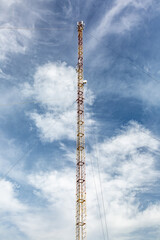 Tall and narrow metal mobile communications tower cell site against the sky with clouds and wires....