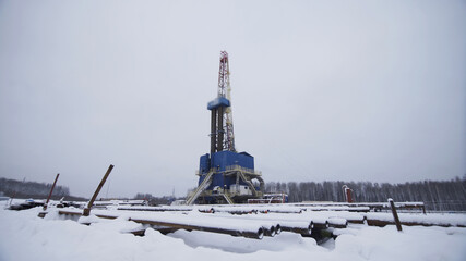Oil and Gas Drilling Rig among snow covered landscape against cloudy sky in winter. Oil drilling rig operation on oil platform in oil and gas industry for drilled in order to produced crude oil