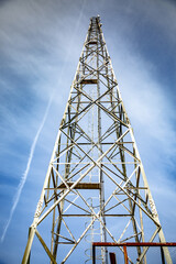 A metal mobile communications tower cell site against a clear sky and a trace from an airplane. Vertical orientation. 