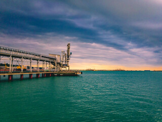 Fototapeta na wymiar Grain pier in the seaport with greenish sea water and cloudy sky.