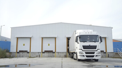 Semi-trailer truck standing at warehouse ramps for load or unload goods at dock logistics park. Truck in parking near warehouse.