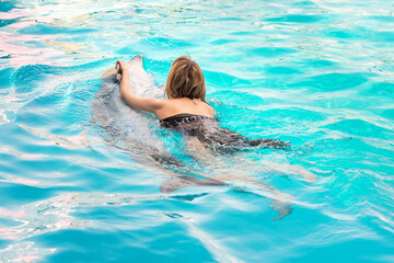 Girl swims in pool with dolphin. Girl swims holding on to dolphin