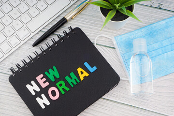 NEW NORMAL text with notebook, safety face mask, keyboard, fountain pen, hand sanitizer and decorative plant on wooden background. Covid 19 and coronavirus concept