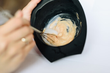 stylist kneads hair dye in a black container close up