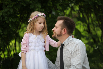 Little sad girl in white dress and wreath of flowers with her father. Dad cheer up his little daughter. Dad's princess. Father's day.