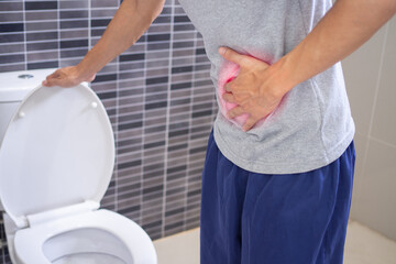 Men are standing with their bellies in front of the toilet in the bathroom. There is severe abdominal pain or diarrhea. Concept of abdominal pain, diarrhea, stomach disease
