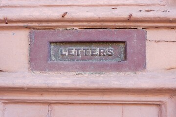Close up on metallic slot for paper letters, newspapers and other correspondence on an old door of pastel colour. Mdina, Malta