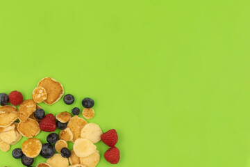 A bowl with mini pancake cerea on green background. Trendy food. Tiny cereal pancakes with blueberries and raspberries. Copy space