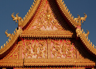 Colorful gable wall flank with golden ornaments and buddha images at a temple site in Siamese Lao PDR, Southeast Asia
