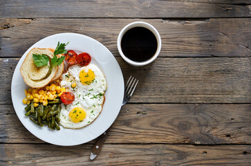 Fried eggs with tomatoes, green beans, corn and toast. English vegetarian breakfast. Top view. Coffee and fried eggs on a wooden tray. Wood background. Free space for text.