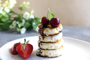 Close-up of cottage cheese pancakes with cherries, curd pancakes or cheese pancakes stacked and decorated with chocolate, horizontal orientation, place for text