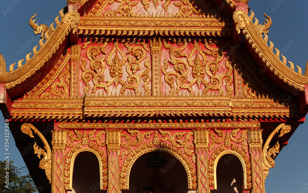 Wall mural colorful gable wall flank with golden ornaments and buddha images at a temple site in siamese lao pd