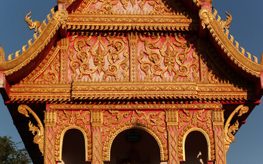 Colorful gable wall flank with golden ornaments and buddha images at a temple site in Siamese Lao...