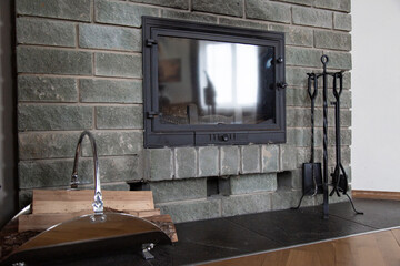 gray brick wall fireplace with traces of black soot. cast-iron fireplace accessories and firewood in a metal basket nearby.