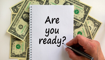 Male hand writing 'are you ready' on white note, on white background. Dollar bills. Business concept, copy space.