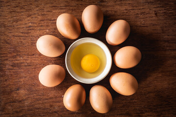 Broken egg shells and raw egg in small bowl line up circle at wooden background for menu and recipe
