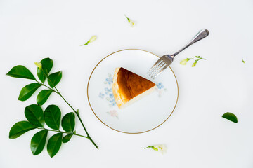 Slice of basque burnt cheesecake on plate with dessert fork on white background, top view.