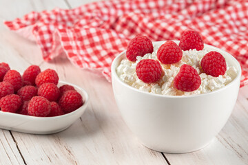 Curd (cottage cheese) wiht fresh raspberries in a white ceramic bowls on a wooden table. Diet breakfast