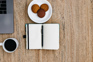 Flat lay, Freelance work laptop smartphone and note pad. Morning coffee with cookies. Copy space on wooden background and notepad.