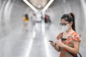 young Asian girl wearing Surgical face mask protect coronavirus inflection, Happy tourist woman using smartphone during walking in subway station. new normal and life after covid-19 pandemic
