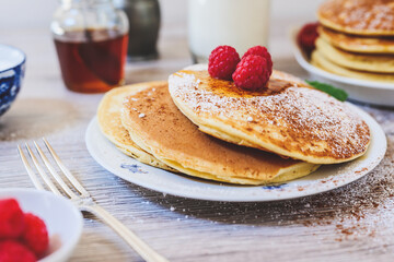 pancakes on white plate with raspberries sugar and syrup