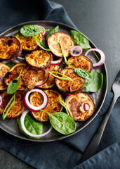Salad with grilled eggplant, spinach, purple onion and sauce on a dark table.