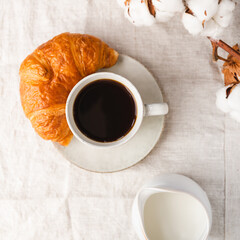 Cup of espresso coffee with croissant on a table with cotton branch.