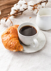 Cup of espresso coffee with croissant on a table with cotton branch.