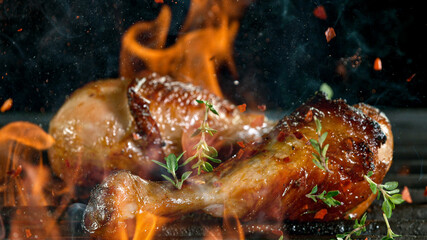 Tasty chicken legs on cast iron grate with fire flames. Freeze motion barbecue concept.