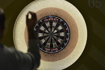 Selective focus shot of a person playing darts placed on a black wall