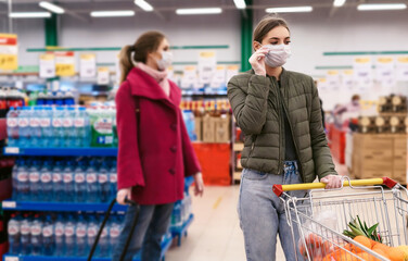 Social distancing in a supermarket. A young women in a disposable face masks and gloves with grocery basket. Shopping during the Coronavirus Covid-19 epidemic 2020