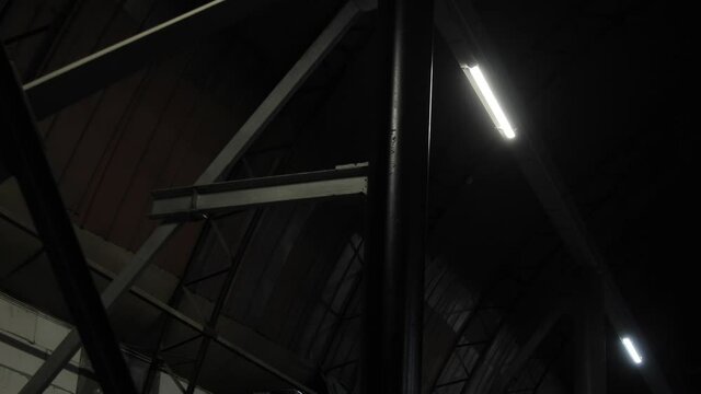 Fluorescent lights lamps on metal beams partitions turn off and turn on in dark room of plant, hangar without windows, workshop department. Power failure, electrical short circuit in industrial area
