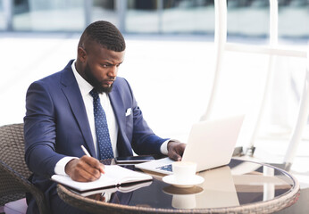 Serious Businessman Working On Laptop Taking Notes In Cafe Outdoor