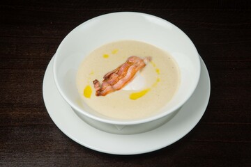 Mushroom cream-soup with bacon and cream .On a white plate. On black background