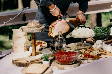 a table in the welcome area with snacks and decor where a person is thinly slicing a large ham