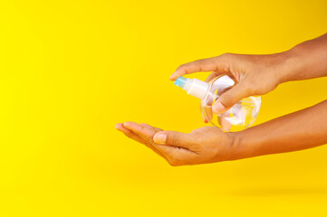 Hand of man applying alcohol spray or anti bacteria spray to prevent spread of virus and bacteria. Applying alcohol spray on hand isolated on yellow background.