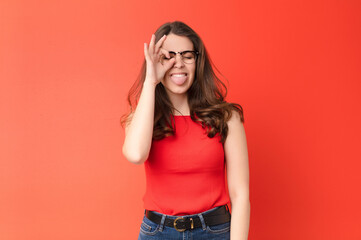 young pretty woman smiling happily with funny face, joking and looking through peephole, spying on...