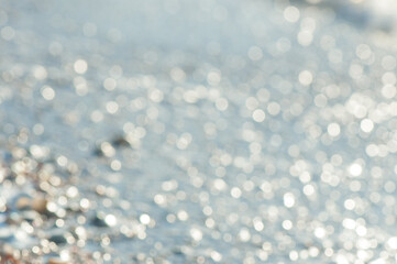 Light blue defocused glitter background with copy space. Sea water glowing abstract backdrop. Blurred bokeh on water surface