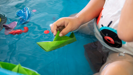 Child hand playing green paper boat in water at home. Preschool learning concept and family activity at home.
