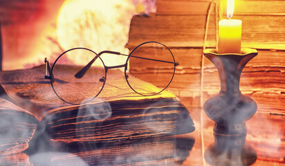 Vintage glasses on an old retro book on a background of the moon. Reading a book by candlelight. The concept of book thrillers and novels.