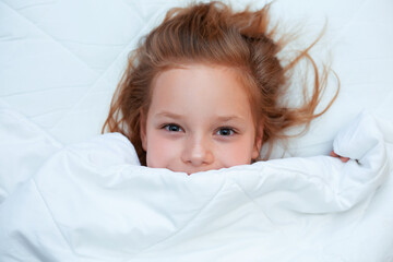 Little red-haired girl lies in a white bed