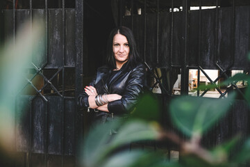 Brunette hipster woman with a positive smile in a leather black jacket posing in the city. Girl model in the Batumi, Georgia. Gates at the background.