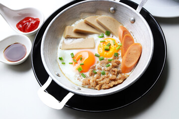 Close up Pan Fried Egg with Toppings served in an aluminum pan with chilli sauce, BBQ sauce on a white table top. Ready to eat