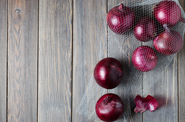 Red onion in the vegetable netting. Wooden brown background. Flat lay, copy space